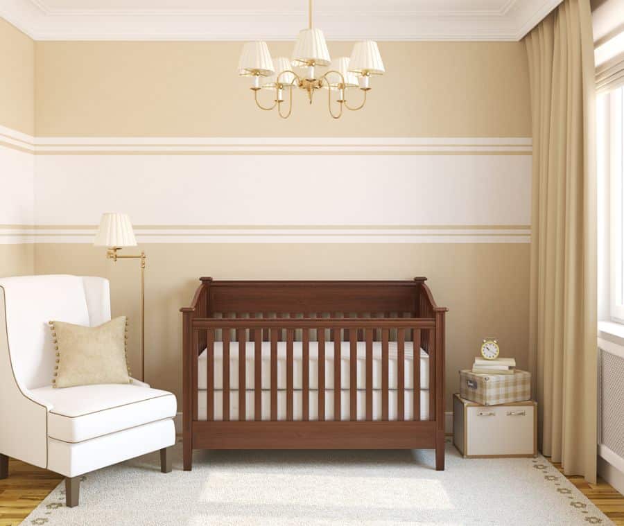 Baby room with dark wooden crib, white armchair, and soft beige tones throughout the decor.