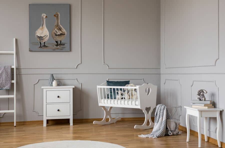 Baby room with a white rocking crib, animal painting, and elegant grey wall paneling.