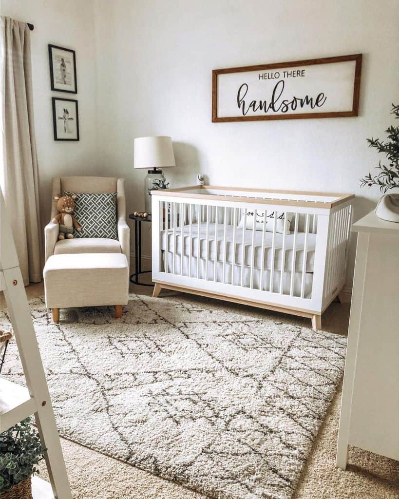 Cozy baby room with a white crib, beige armchair, and decorative wall sign reading "Hello There Handsome".