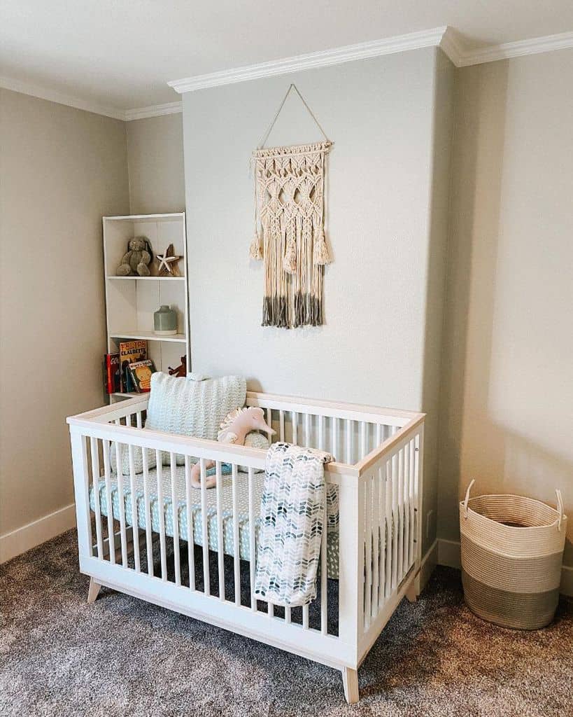 Baby room with white crib, macramé wall hanging, and cozy grey carpet.