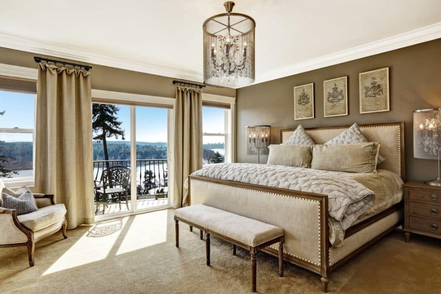 Elegant bedroom with chandelier, upholstered bed, and balcony view.