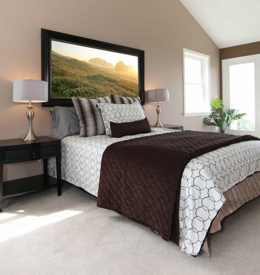 Neutral bedroom with nature wall art, dark bedding, and matching bedside lamps.