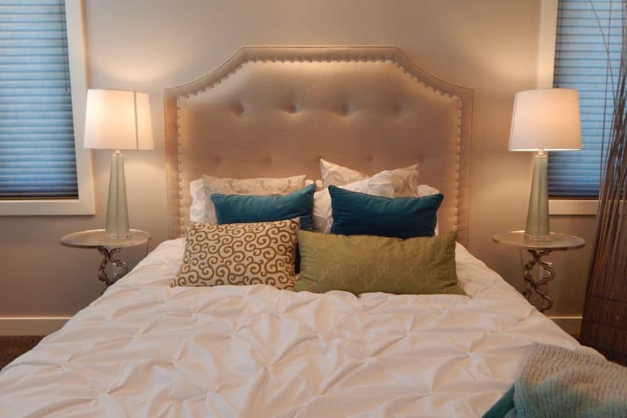 Beige bedroom with tufted headboard, colorful throw pillows, and glass bedside lamps.