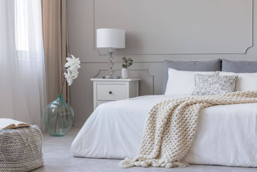 White bedroom with platform bed, textured throw, and glass vase decor.