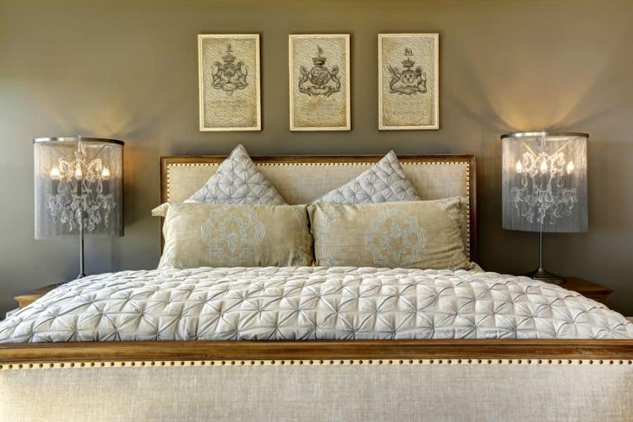 Elegant bedroom with upholstered bed, chandelier lamps, and framed wall art.