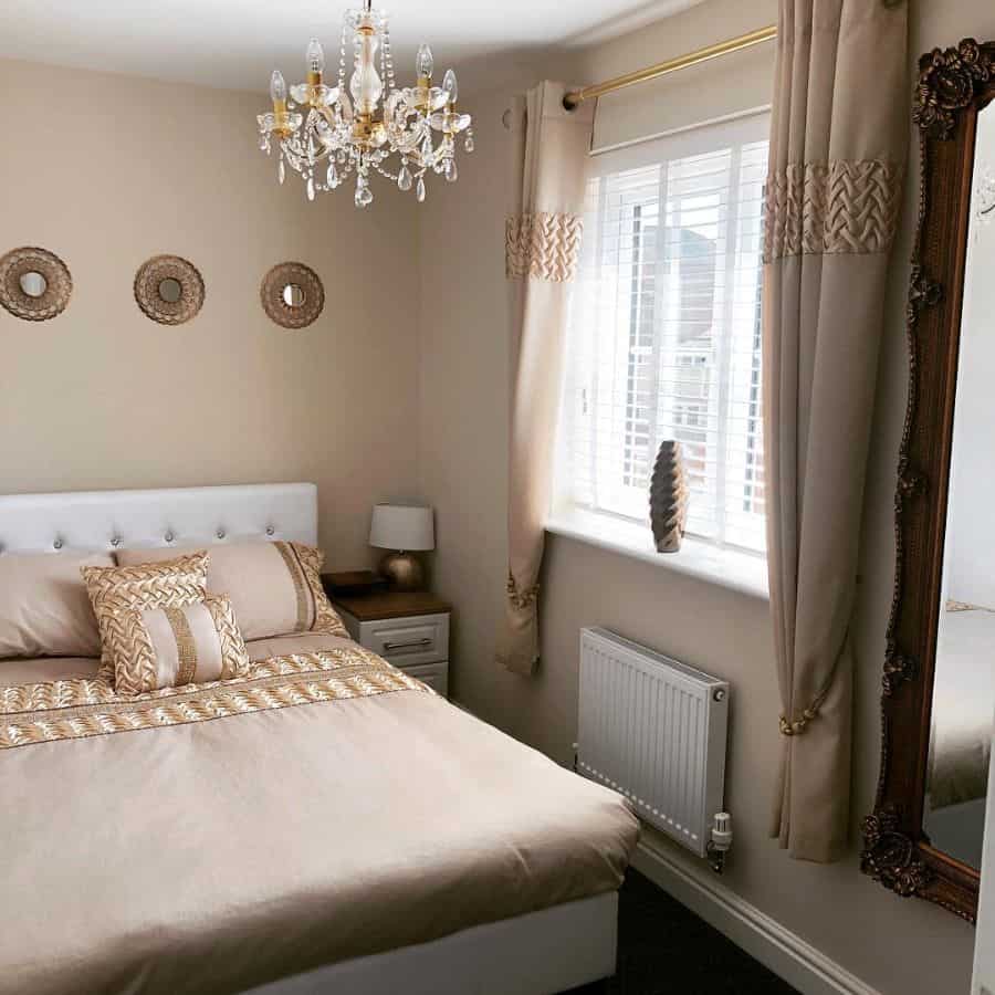 Regal bedroom with crystal chandelier, ornate mirror, and beige decor accents.