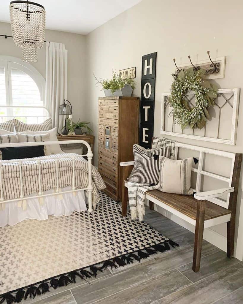 Farmhouse bedroom with metal bed, wood bench, tall dresser, and rustic decor.