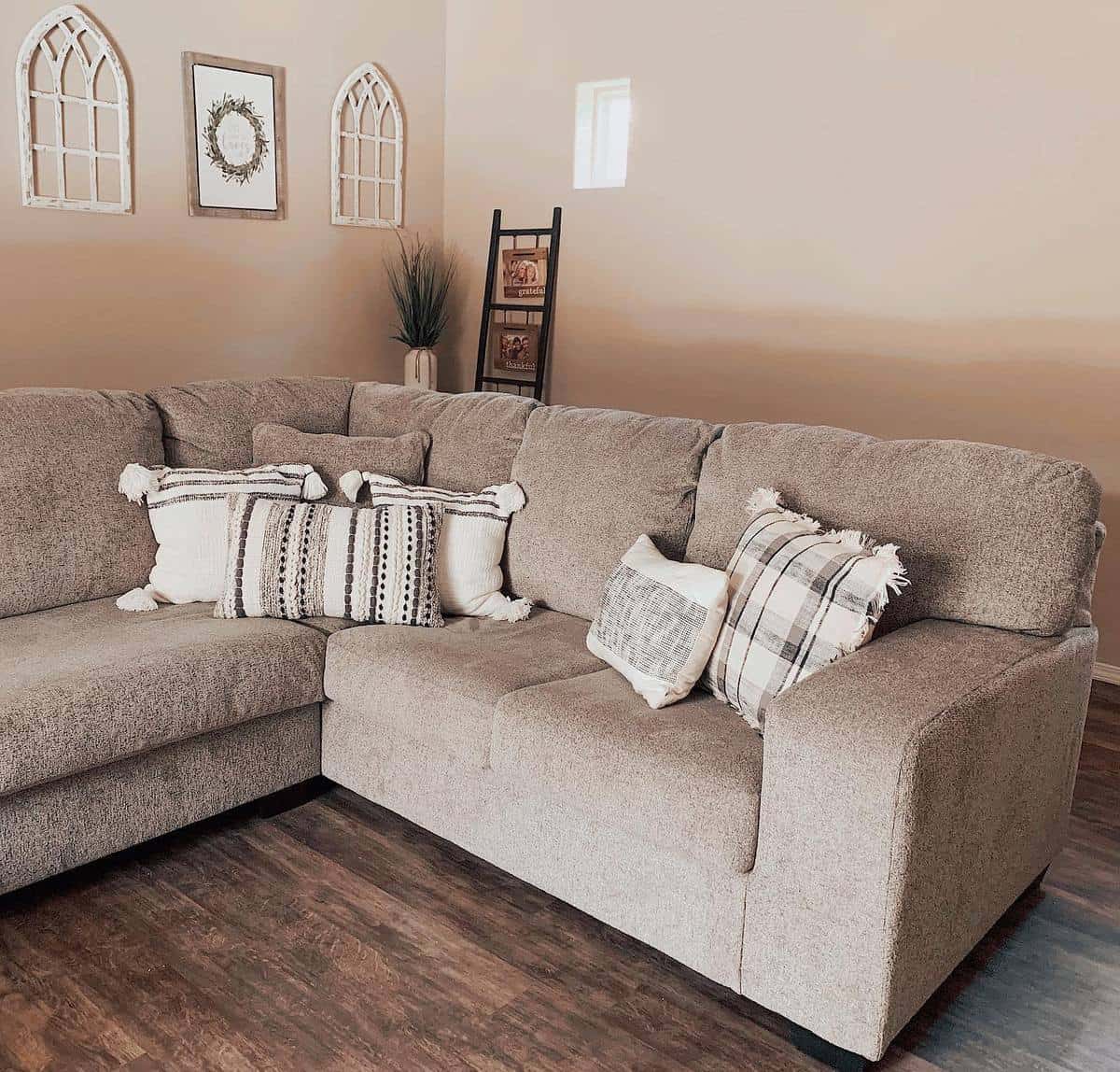 A cozy living room with a brown sectional sofa, decorative pillows, and wall art on a wooden floor