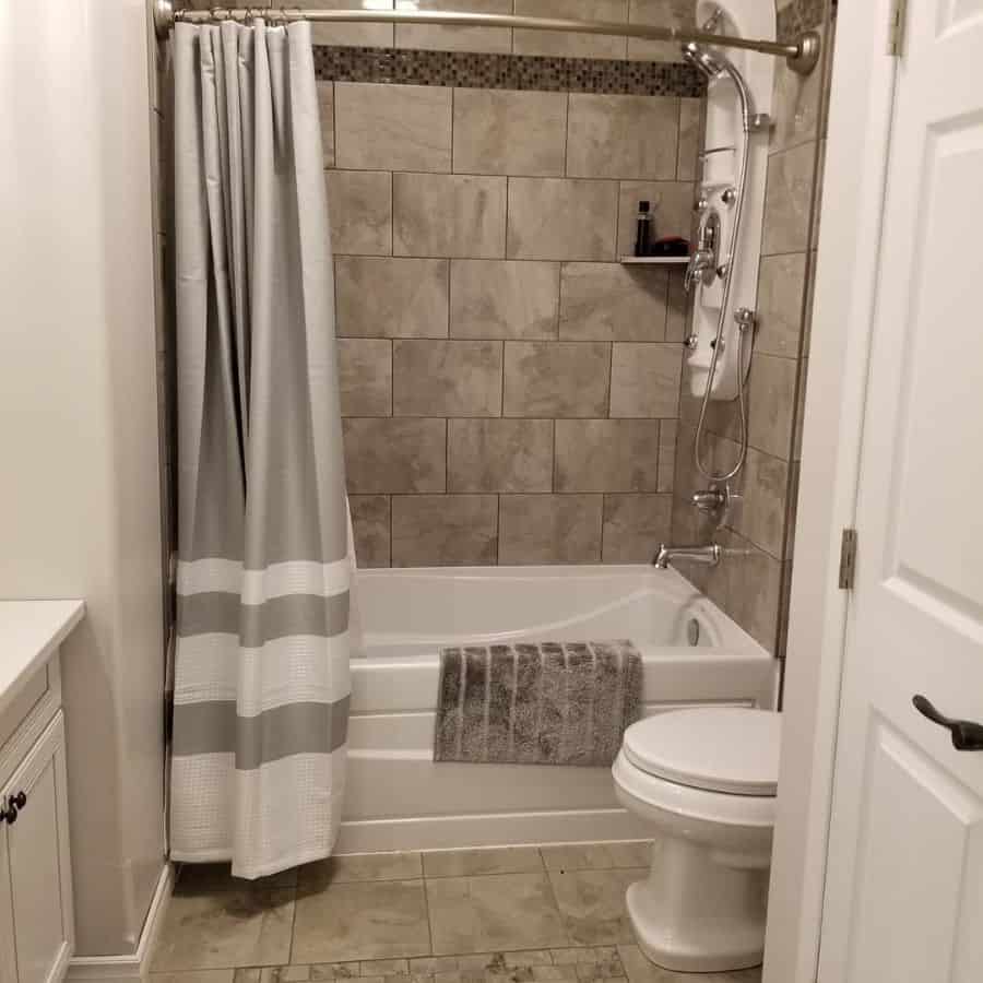 Neutral-colored basement bathroom with tiled shower, bathtub, and striped shower curtain.