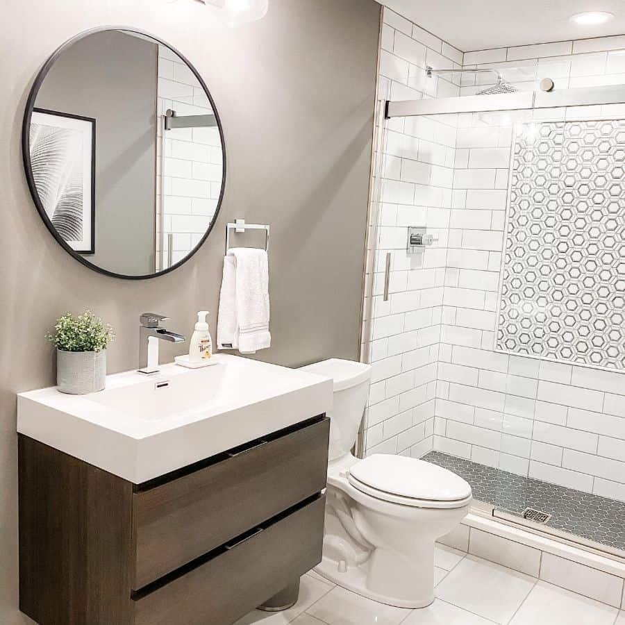 Modern bathroom with floating vanity, round mirror, and glass-enclosed shower with tile accents.