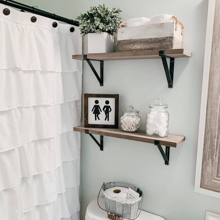 Wooden shelves above toilet with jars, bathroom decor, tissue box, and small plant.