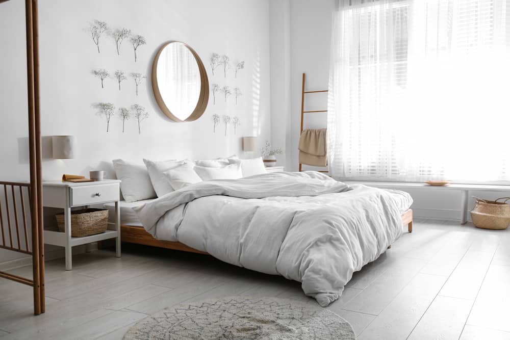 Minimalist bedroom with a cozy bed, round mirror, and natural light; white accents and simple decor create a tranquil vibe