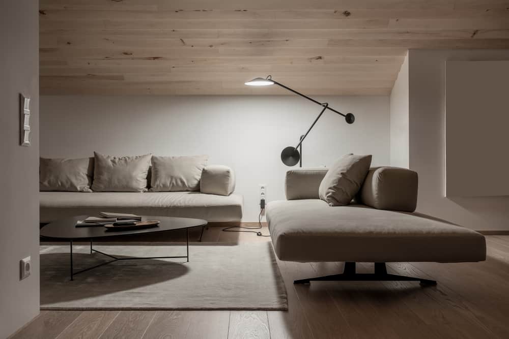 Cozy neutral-toned minimalist living room with low lighting, soft beige furniture, a sleek black coffee table, and a modern wall-mounted lamp accentuating the serene ambiance