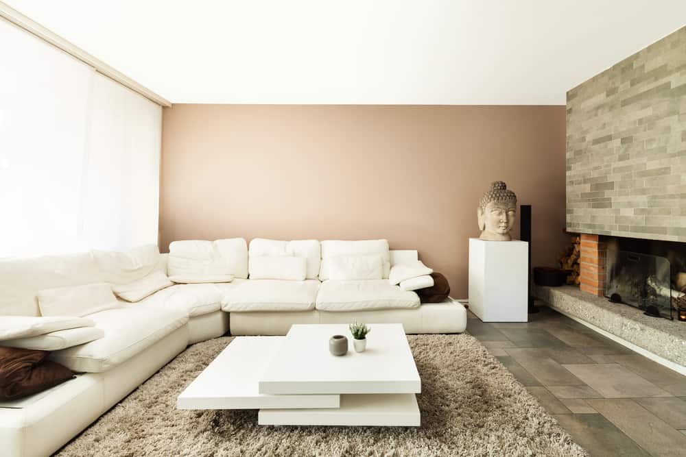 Cozy neutral living room with a beige sectional, textured rug, stone fireplace, layered tables, and a serene Buddha statue accent