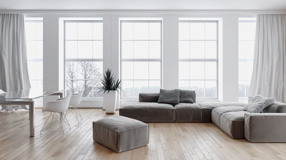 Bright and airy living room with large windows, gray modular sofa, light wood flooring, and a simple dining area in a neutral palette