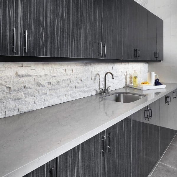 Contemporary kitchen with white textured stone backsplash, gray cabinets, and sleek countertop.