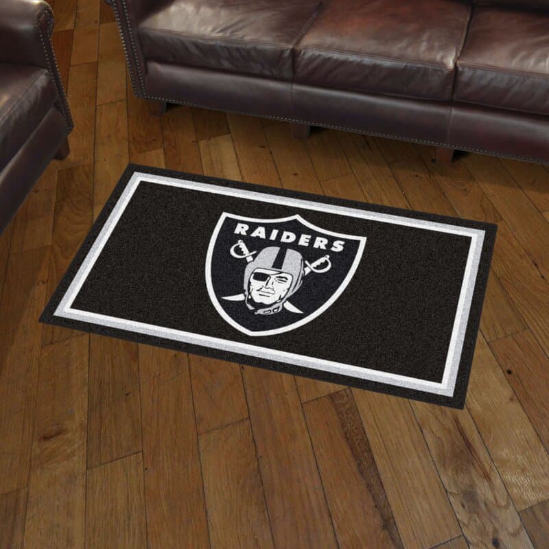 Raiders logo rug on wooden floor between two brown leather sofas.