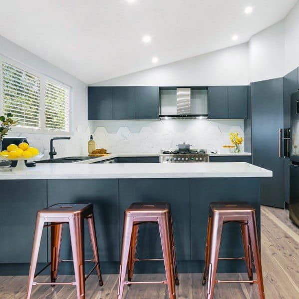 Modern black kitchen with white countertops, wooden stools, and hexagon backsplash tiles.