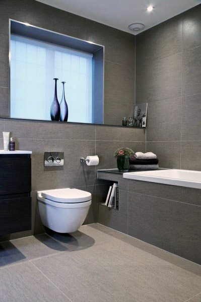 Modern bathroom with grey tiles, a toilet, and a bathtub adorned with towels and vases