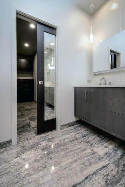 Modern bathroom featuring a sleek black pocket door with a full-length mirror, gray cabinetry, and marble-patterned flooring