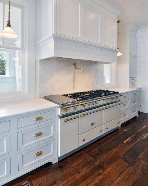 This kitchen showcases a luxurious design with clean white cabinetry and striking hardwood flooring, complemented by a high-end gas stove and brass hardware for a sophisticated, timeless look