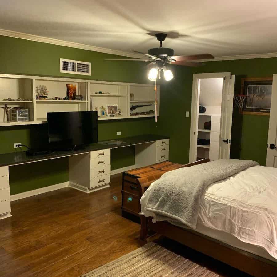 Bedroom with green walls, built-in shelves, large desk, and ceiling fan.