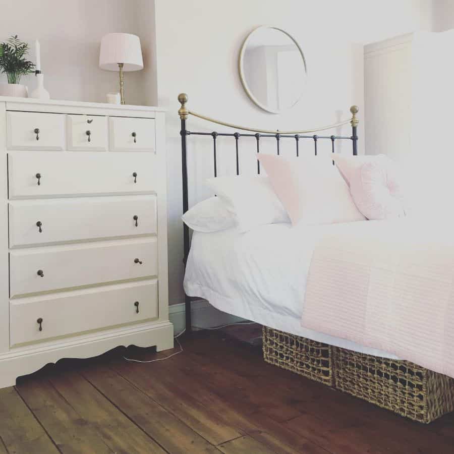 Bright bedroom with iron bed frame, white chest of drawers, and wicker storage baskets.