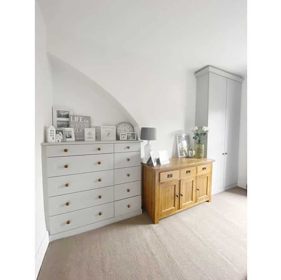 Bedroom with white and wooden dressers, framed photos, and neutral decor.