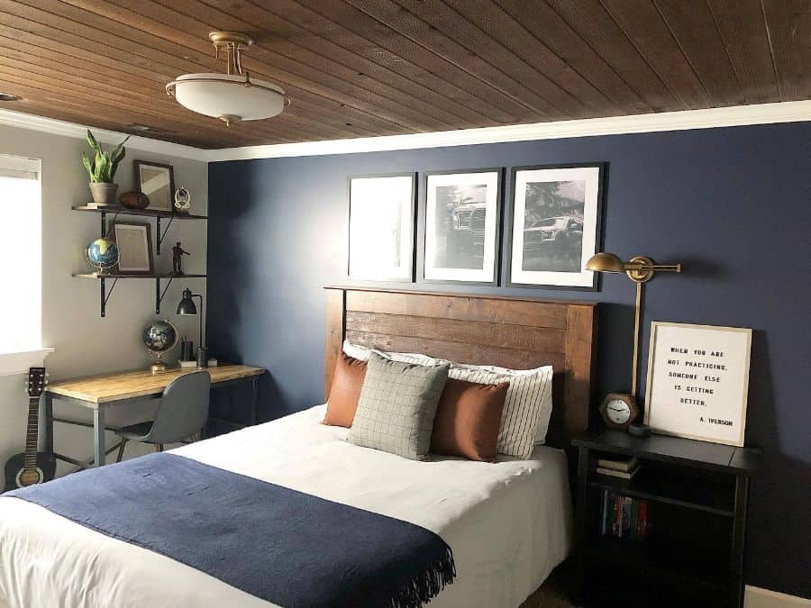 Modern bedroom with navy accent wall, wooden headboard, and small desk setup.