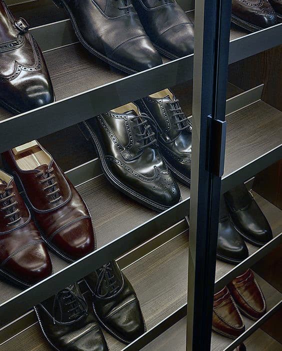 A glass cabinet displaying polished brown and black leather dress shoes on wooden shelves