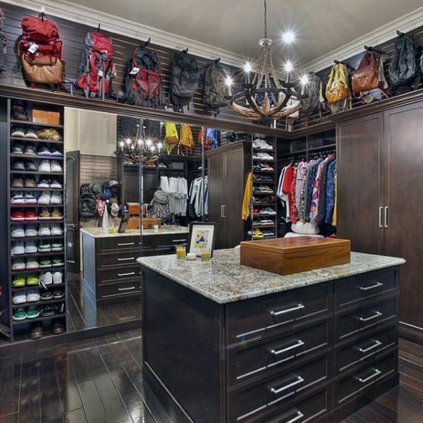 Spacious walk-in closet with shoe shelves, hanging clothes, backpacks, and a central island with drawers under a chandelier