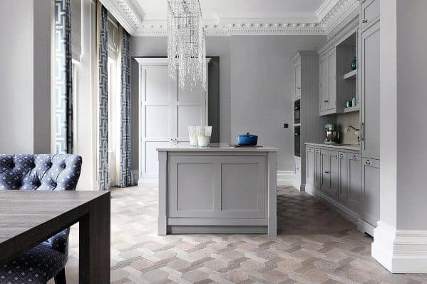 This elegant kitchen features an ornate herringbone hardwood floor pattern, complemented by soft gray cabinetry and luxurious chandeliers, creating a sophisticated and timeless atmosphere