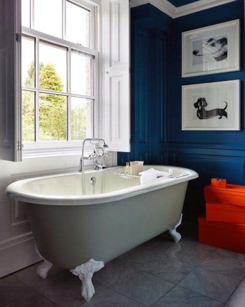 Classic bathroom with navy walls, clawfoot bathtub, large window, and framed dog art.