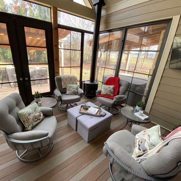 Cozy enclosed patio with plush swivel chairs, a wood stove, large windows, and a warm atmosphere for year-round relaxation