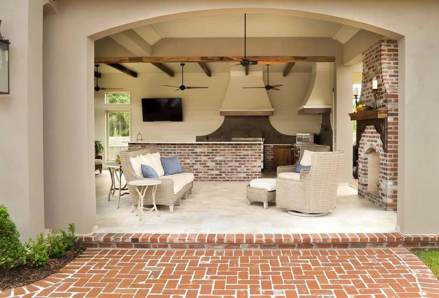 Elegant outdoor kitchen with a brick bar, rustic wooden beams, ceiling fans, and a cozy seating area, combining modern comfort with timeless charm