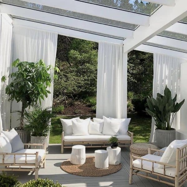 Bright and airy outdoor seating area with white furniture, natural wood accents, and lush greenery under a glass roof