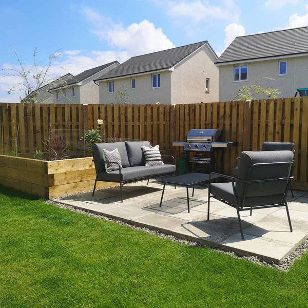 Simple and inviting backyard patio setup with modern metal furniture, a barbecue grill, and lush green lawn