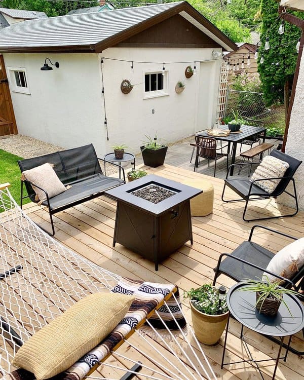 Cozy backyard deck featuring a fire pit, stylish metal chairs, potted plants, and a relaxing hammock for a laid-back outdoor retreat