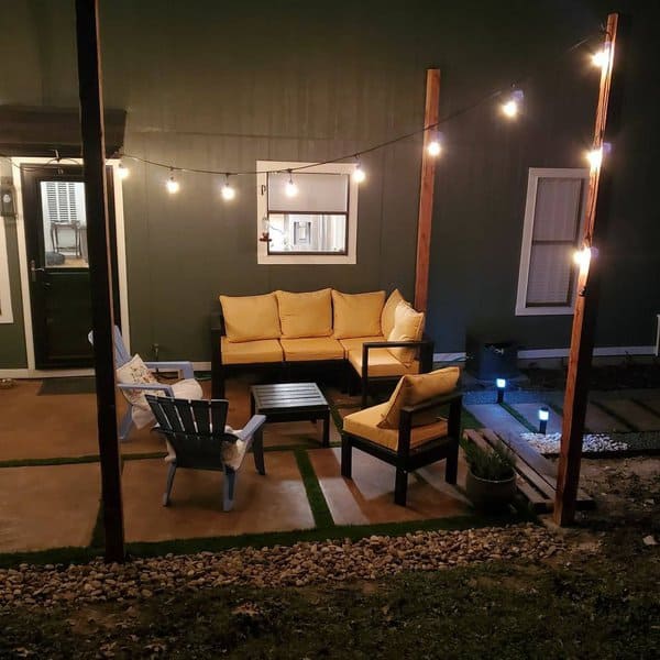 Intimate backyard retreat with warm yellow cushions, string lights creating a cozy glow, and a minimalist patio design for relaxed evenings