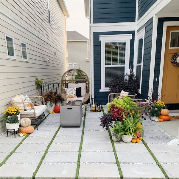 Charming side patio with modern concrete pavers, lush plants, cozy seating, and seasonal decor featuring pumpkins for a festive touch