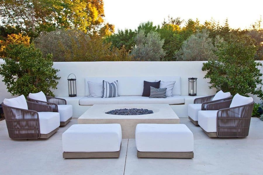 Modern outdoor seating arrangement with a minimalist firepit, white cushions, and cozy greenery in a serene garden setting