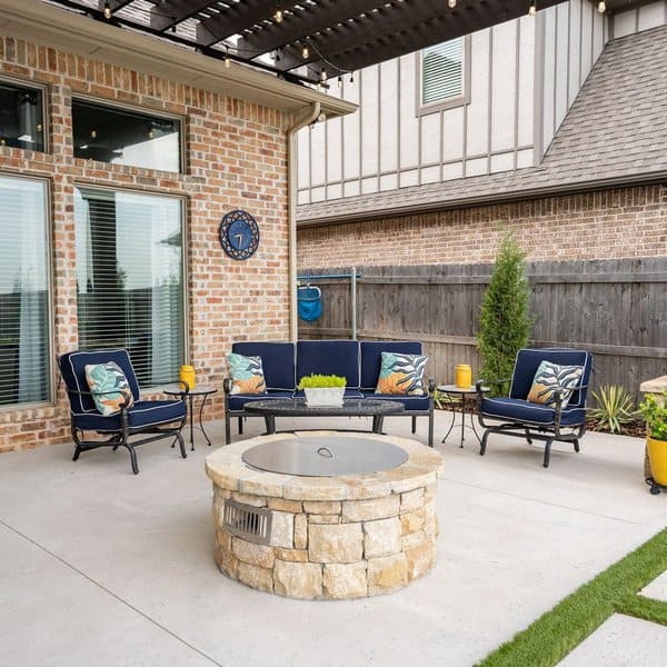 Stylish patio with blue seating, floral pillows, stone firepit, and lush accents, perfect for cozy evenings outdoors