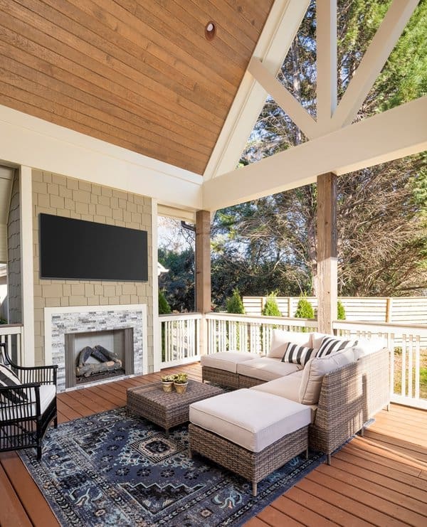 Covered patio with a high vaulted ceiling, cozy sectional, patterned rug, and a built-in fireplace with a mounted TV for entertainment