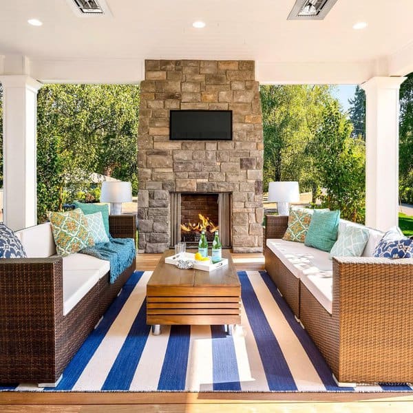 Elegant outdoor lounge with a stone fireplace, vibrant striped rug, and cozy wicker seating for year-round relaxation