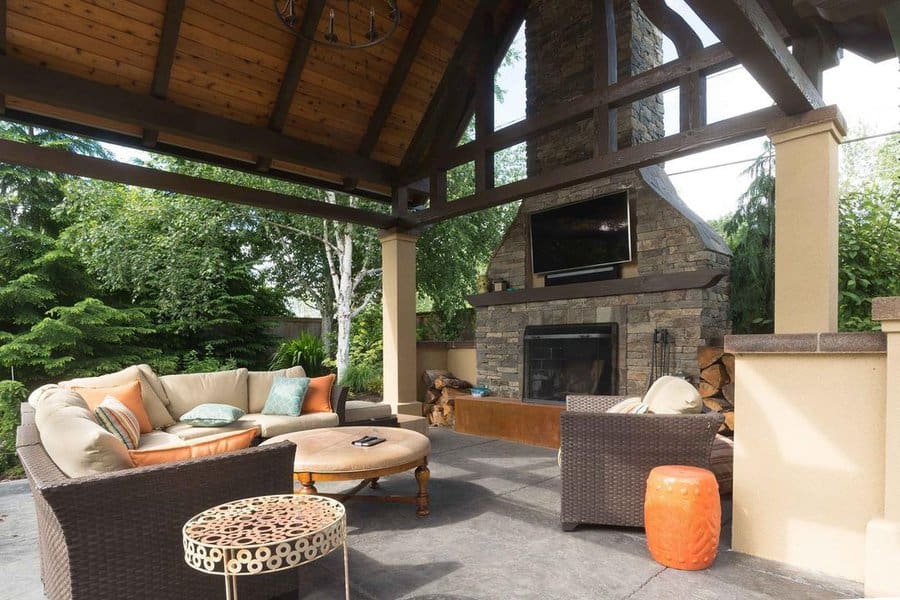 Cozy covered patio with a stone fireplace, rustic wood beams, and inviting wicker furniture for ultimate outdoor comfort