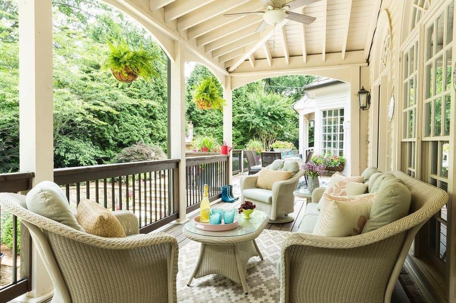 Inviting porch with comfortable wicker seating, pastel cushions, and hanging ferns, creating a serene atmosphere surrounded by lush greenery