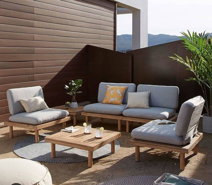 Modern outdoor seating area with wooden furniture, minimalist cushions, and tropical plants, creating a cozy yet contemporary vibe