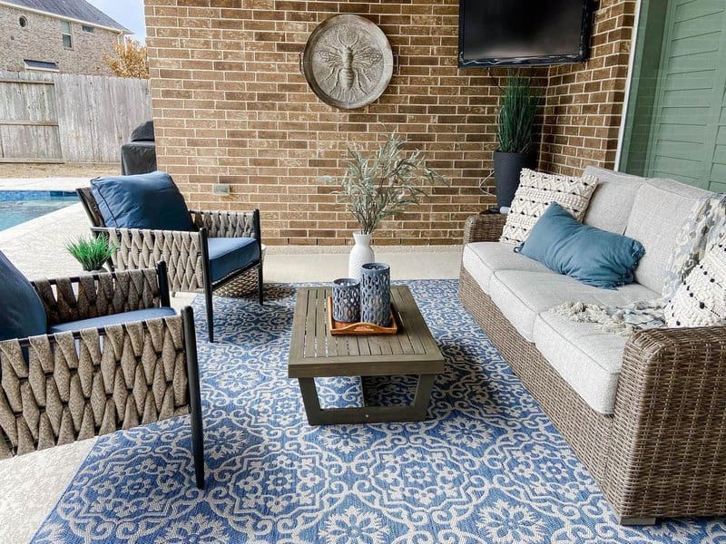 Charming outdoor seating area featuring woven furniture, a patterned blue rug, and accents like decorative pillows and a modern coffee table, perfect for poolside relaxation