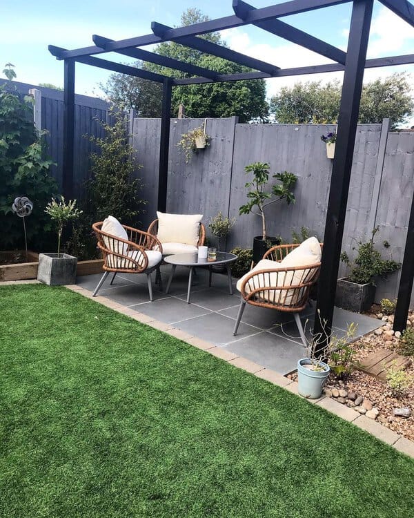 Charming garden nook featuring a pergola-covered seating area with cozy rattan chairs, a small round table, and lush greenery, creating a serene and inviting outdoor retreat