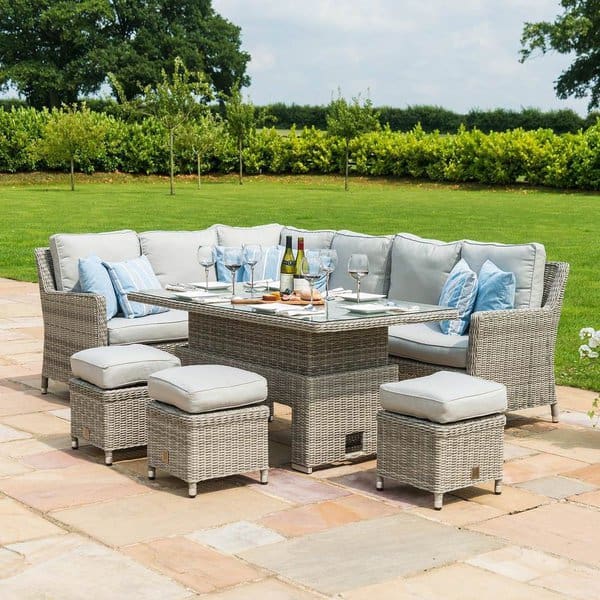 Charming outdoor dining setup featuring a wicker sectional with soft gray cushions and matching stools, arranged around a glass-top table, set on a stone patio overlooking a lush green garden